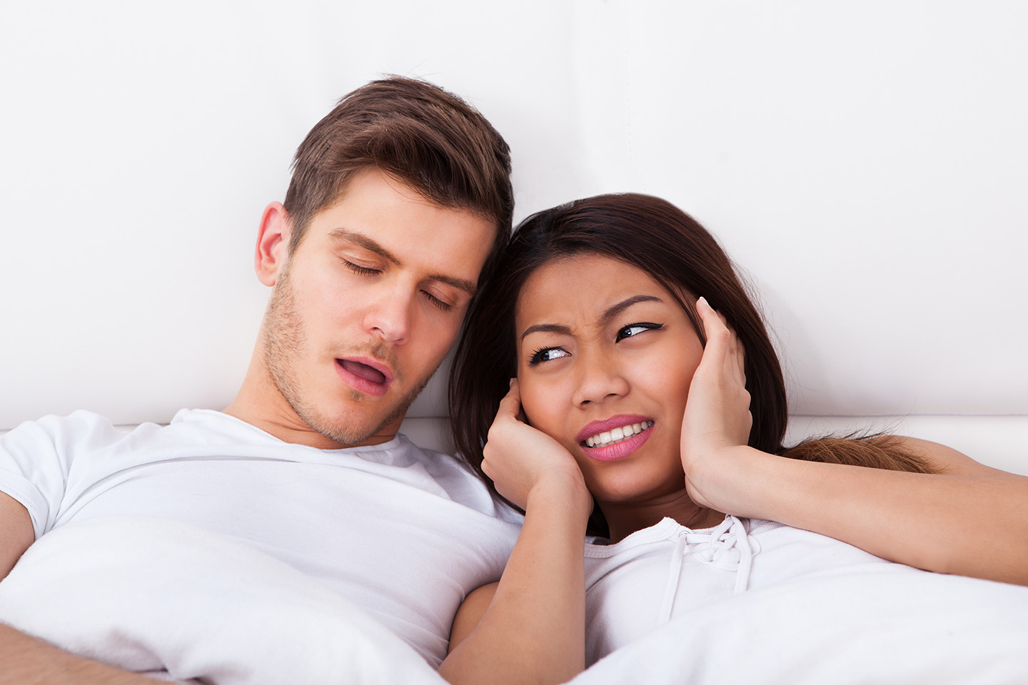 Couple sleeping while wife is awake muffling her ears.